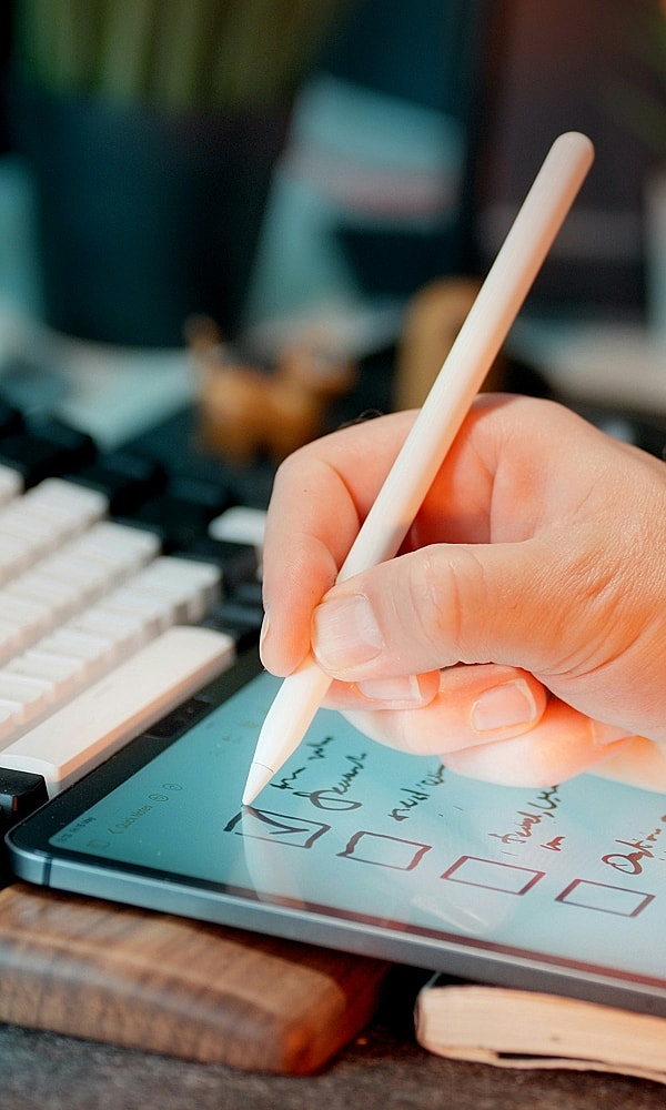 Hand using stylus on tablet with notes.