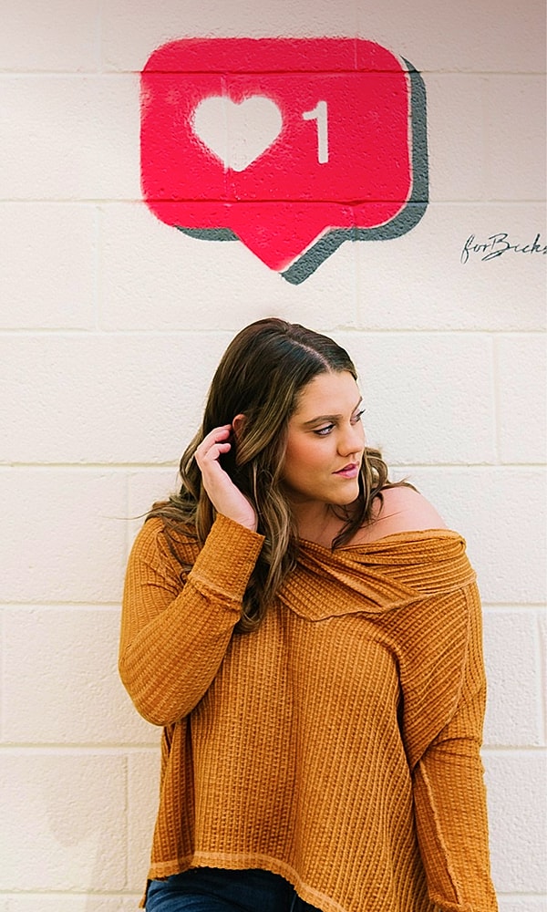Woman posing beside heart-shaped social media icon.