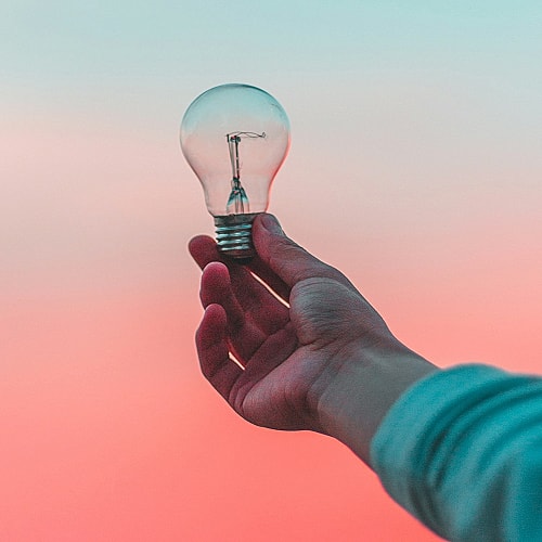 Hand holding a light bulb at sunset.