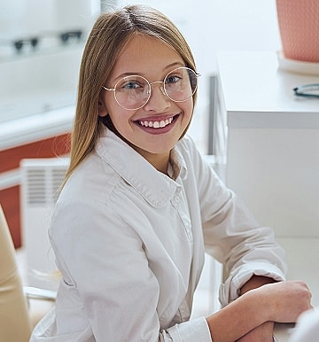 Girl smiling, wearing glasses, at a desk.