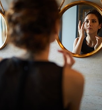Woman applying skincare in front of mirrors.