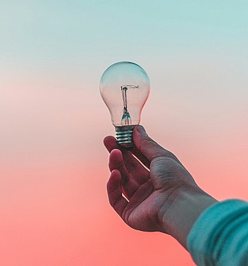 Hand holding a light bulb against colorful background.